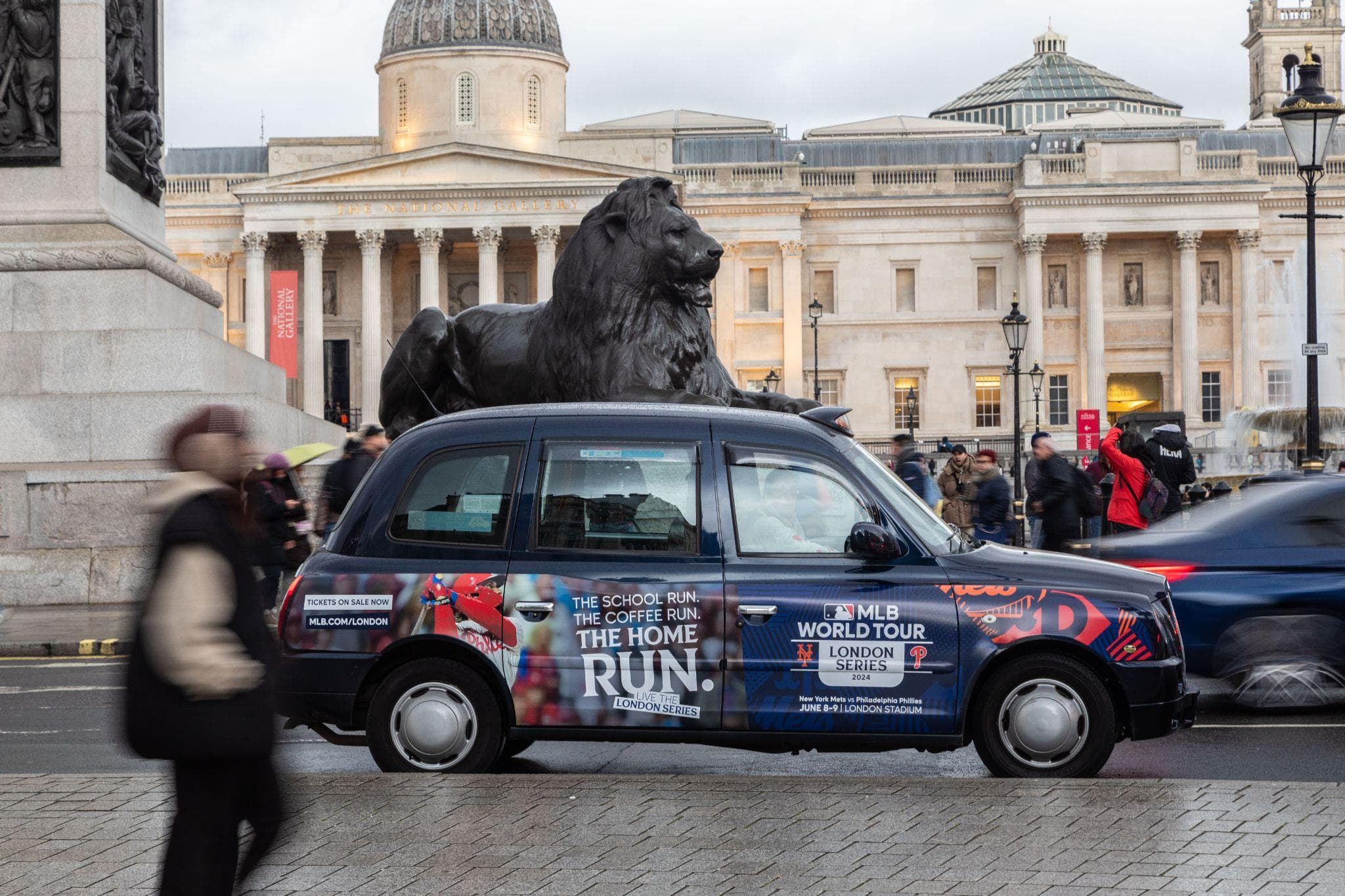 A Major League Baseball superside panel on a classic black cab passing the lions at Trafalgar Square