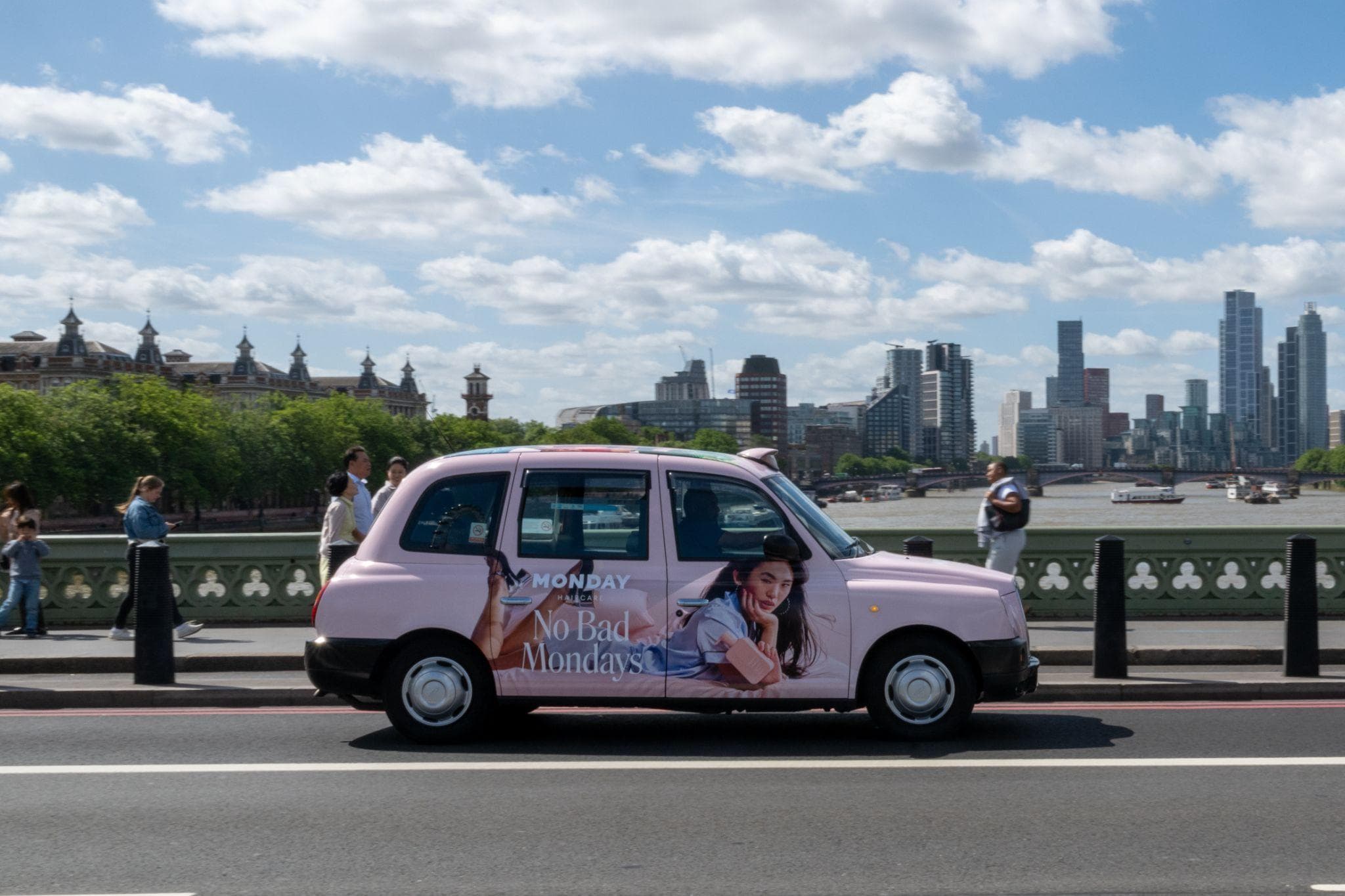 A pink Monday Haircare No Bad Mondays full wrap on a classic black cab crossing Westminster Bridge