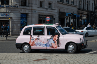 Classic London black cab wrapped in a full vinyl livery, photographed outside a city-centre station